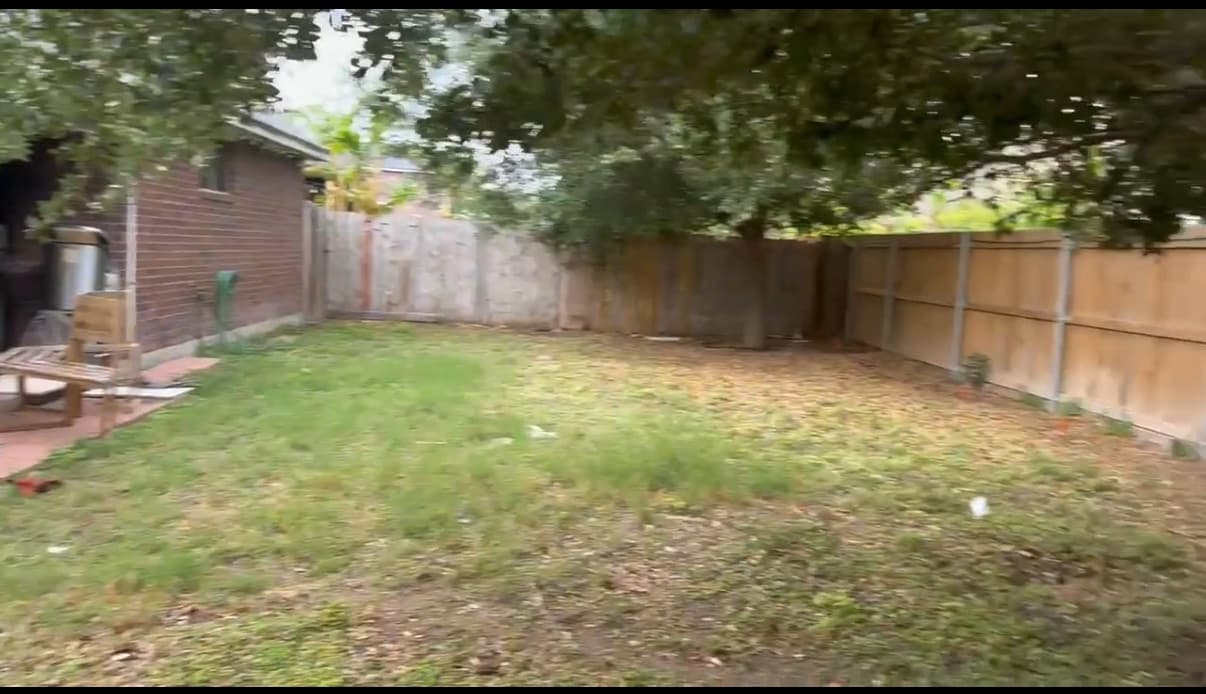 The same backyard before construction: patchy lawn and old fence